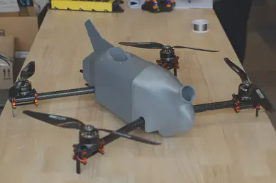 The grey quad-rotor Coptersonde sits on a light wooden benchtop. The instrument scoop is pointed toward the camera.